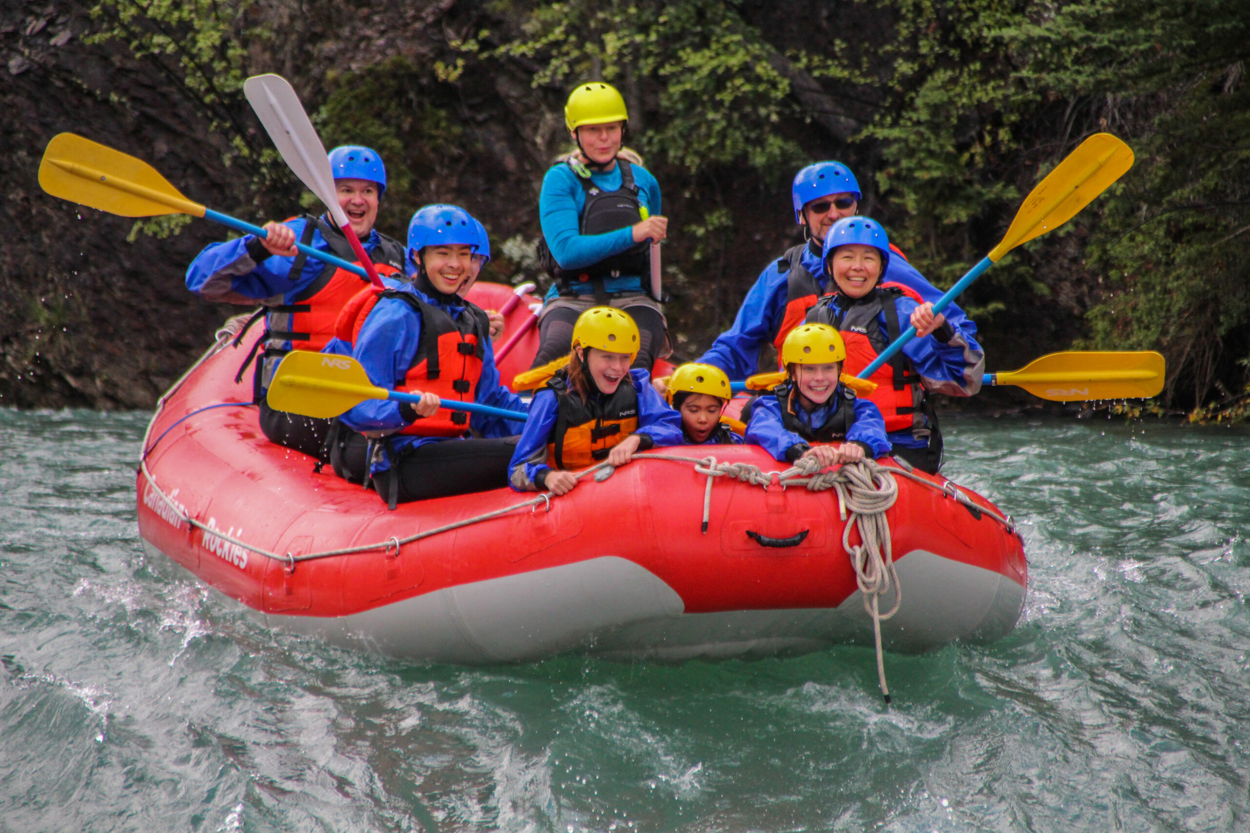 Group of smiling and excited adults, youth and children Whitewater Rafting in a red raft
