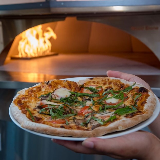 Forno-fired oven with a freshly made margarita pizza in the foreground.  Great for family dining.
