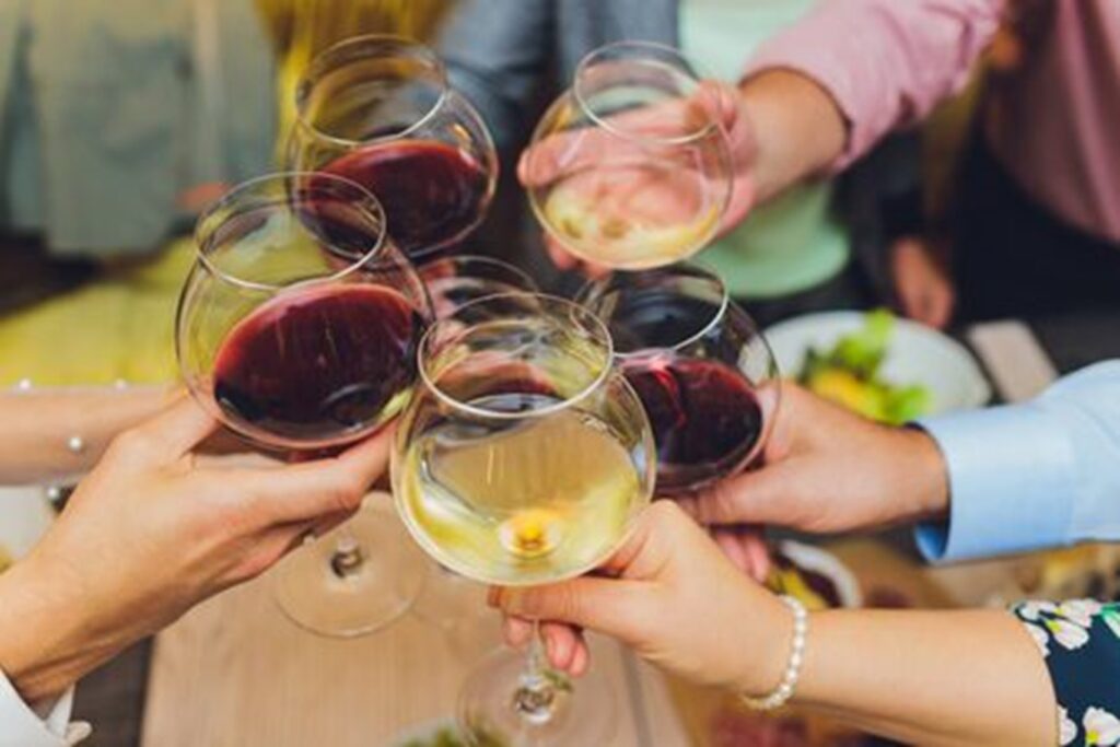Five wine glasses full of red and white wine, coming together for a cheers.  